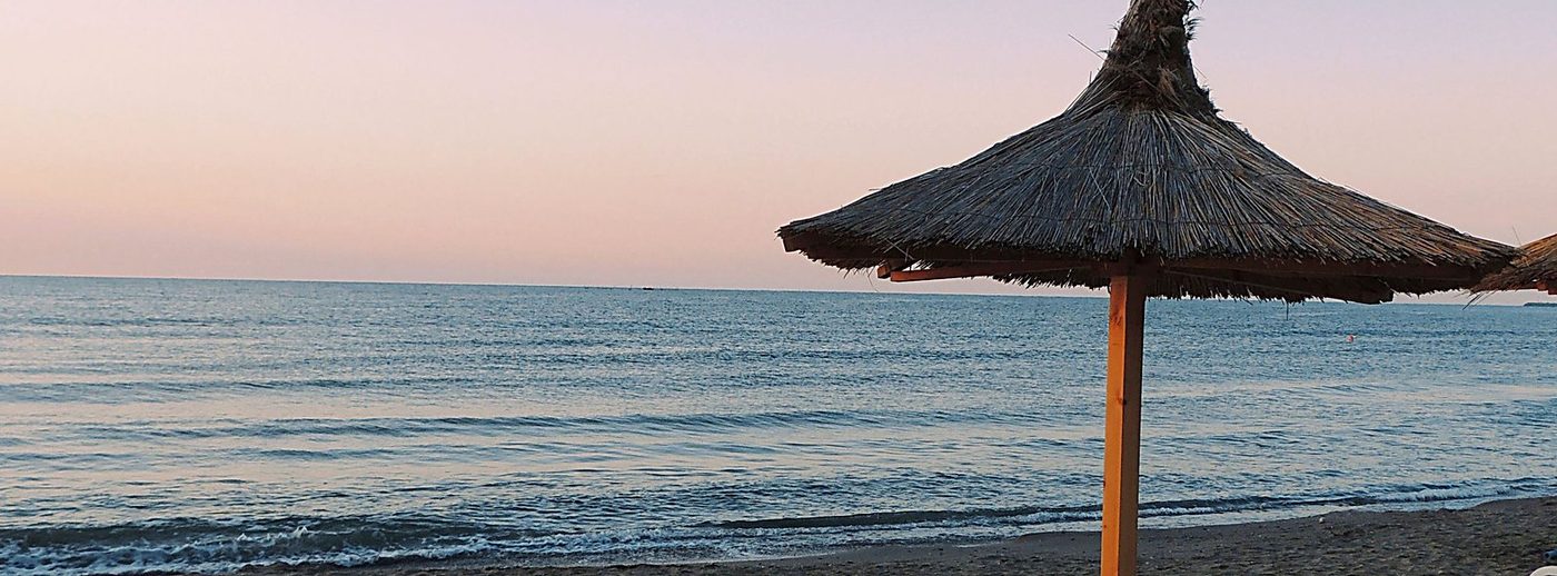 Plajă la Marea Neagră în zori, cu o umbrelă de paie