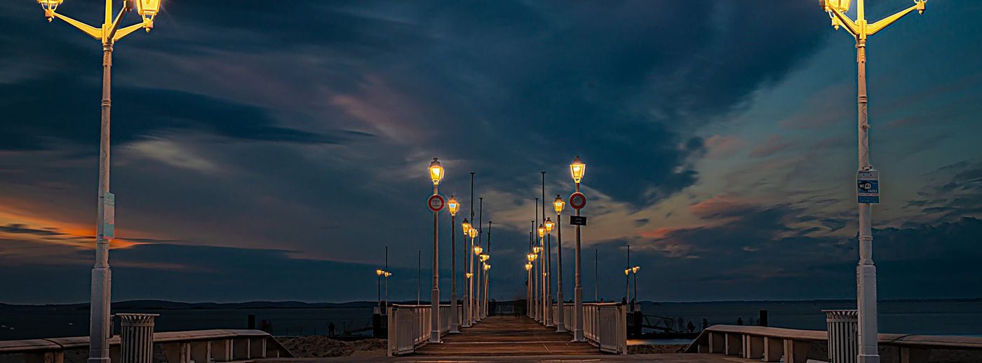 Ponton luminat la malul mării, în amurg