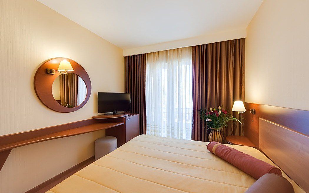 Cameră la Hotel Palas: pat, birou cu televizor, oglindă și fereastră spre grădină